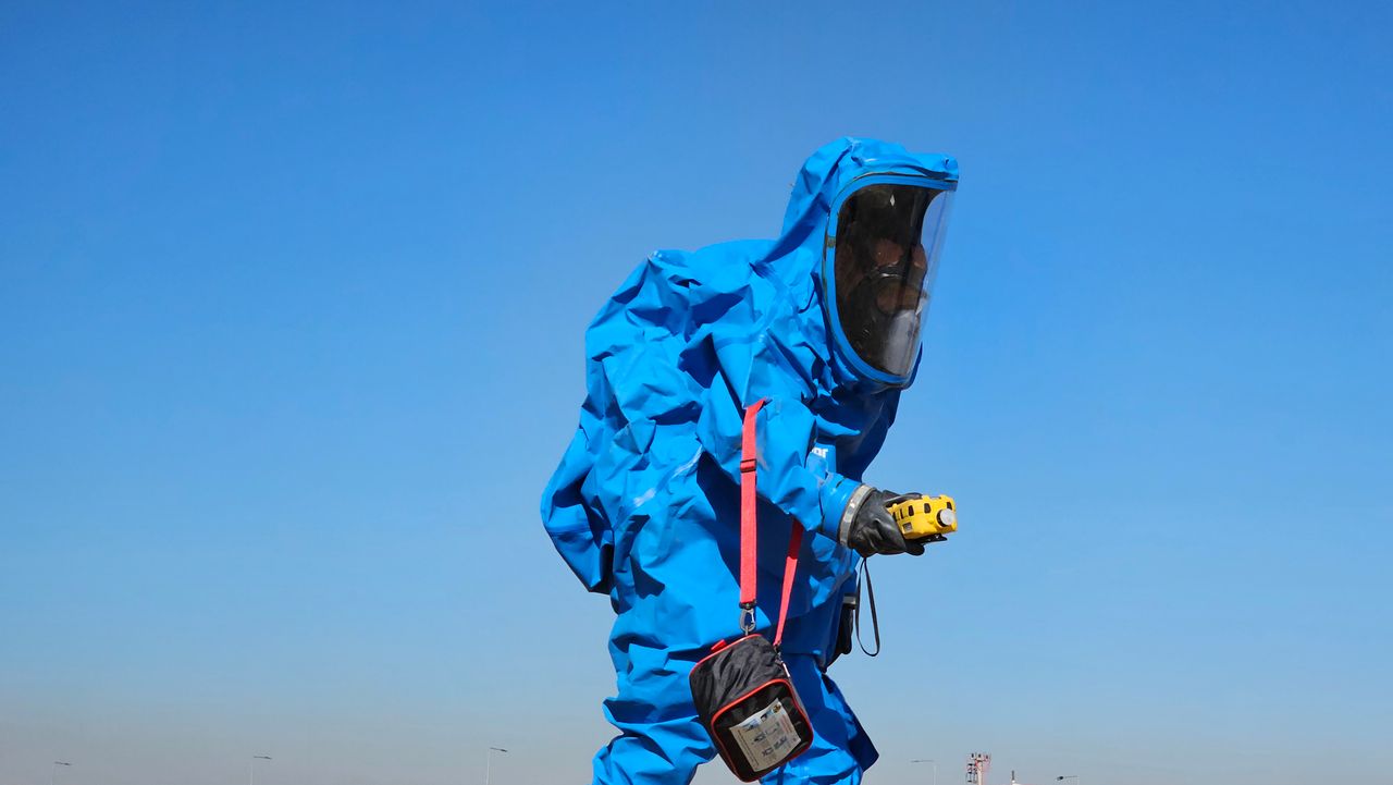 Protective hazmat suit worn by individual inspecting outdoors during daylight.