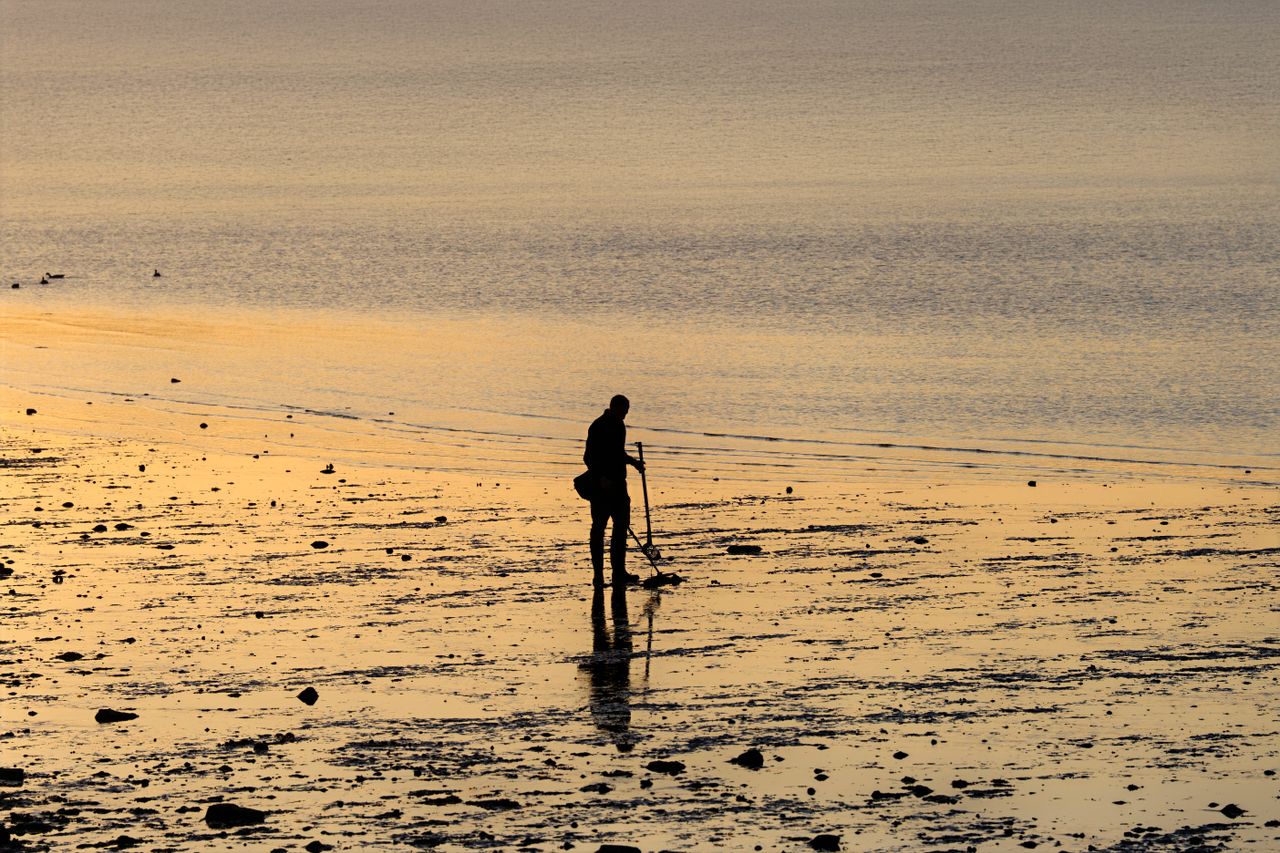 Silhouette of a person metal detecting on a tranquil beach at sunrise, Stamford, Connecticut.